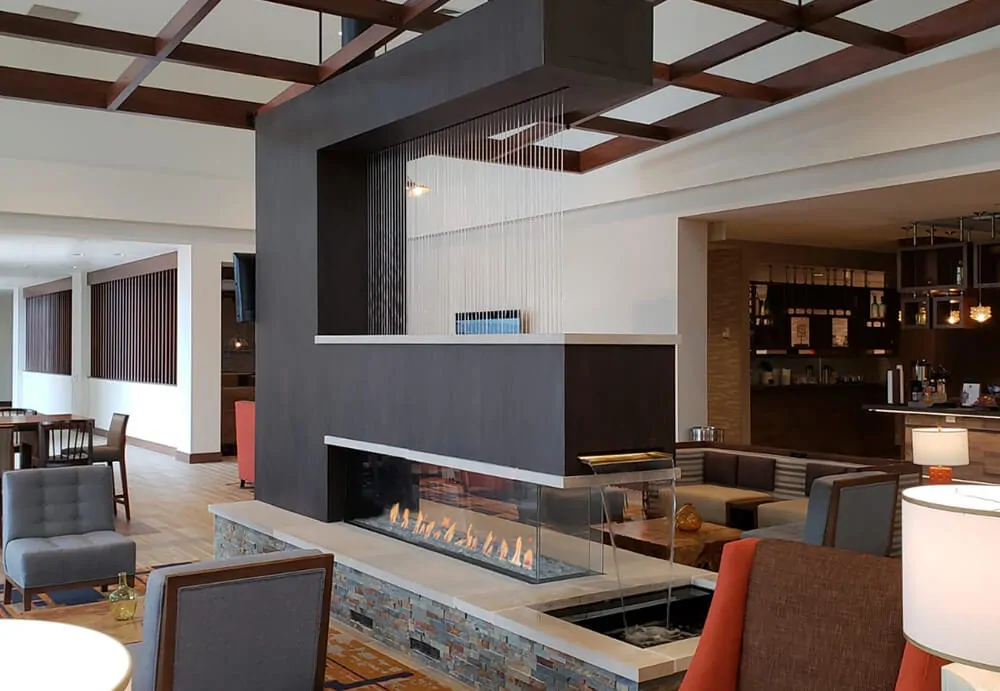 Large three sided gas fireplace in a hotel lobby: Flare Room Definer with seating on both sides.