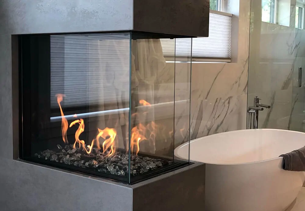 Three sided fireplace in a modern bathroom: Flare Room Definer 45-H with wrap-around glass beside a freestanding bathtub.