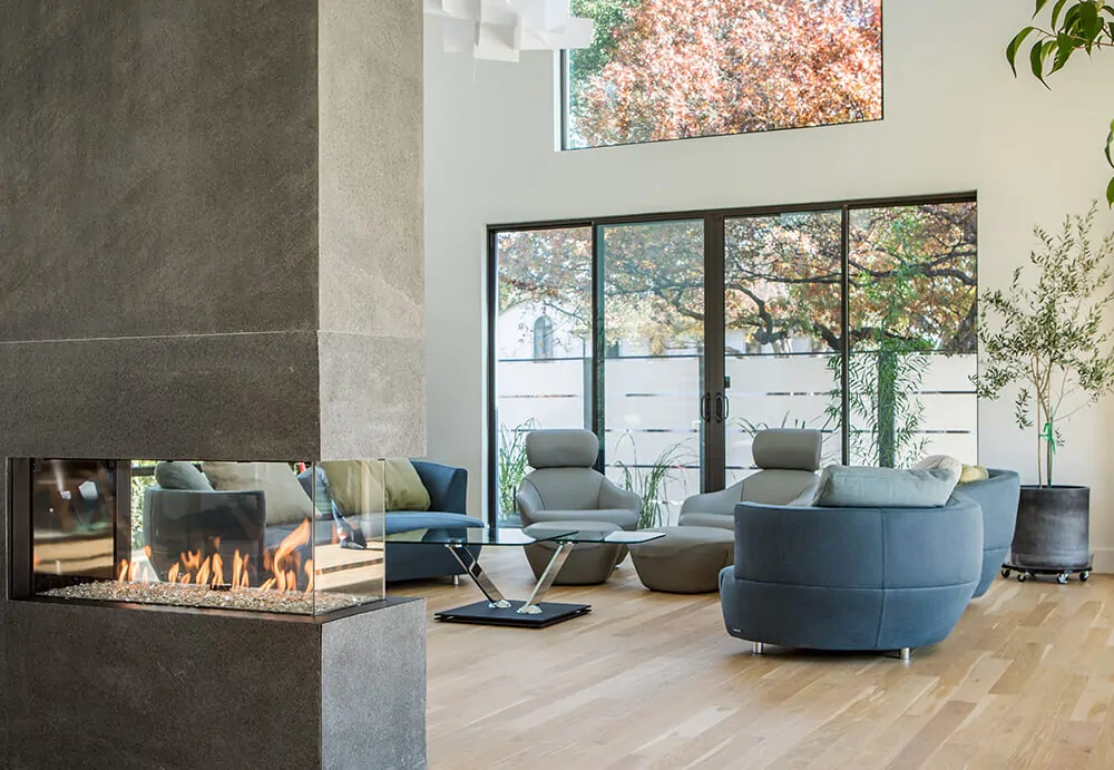 Modern living room with a three-sided glass Flare Room Definer 60" Modern Indoor Fireplace with large windows. FLARE-RD-60