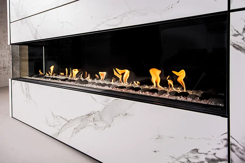 Sleek linear Flare Left Corner 100" Modern Commercial Fireplace with Cool Touch Double Glass, integrated into a white marble wall with vibrant flames.