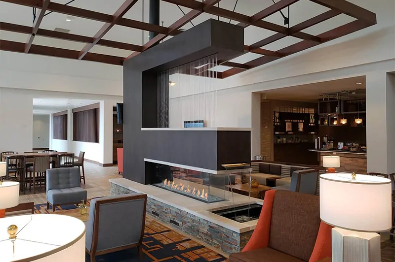 Hotel lobby with a modern suspended Flare Room Definer 100" Modern Commercial Fireplace with Cool Touch Double Glass, and stylish seating arrangements.