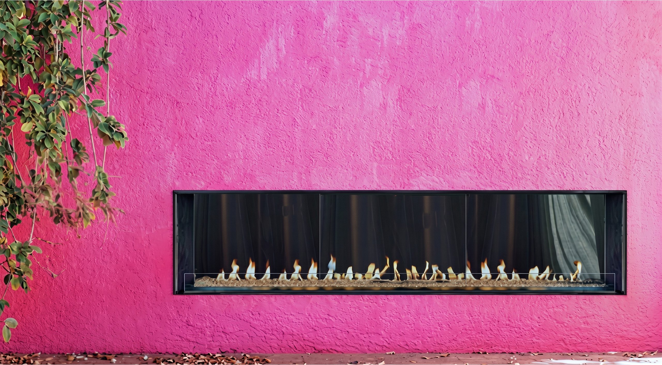 Long black-framed fireplace with a row of flames inset into a bright pink stucco wall beside trailing green foliage.