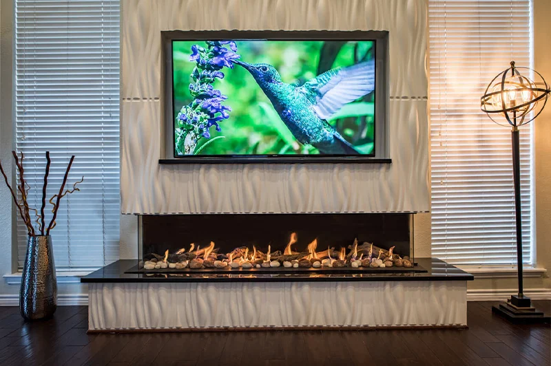 Three sided gas fireplace: Flare Double Corner 80 in a textured surround with mounted TV and ambient lighting.