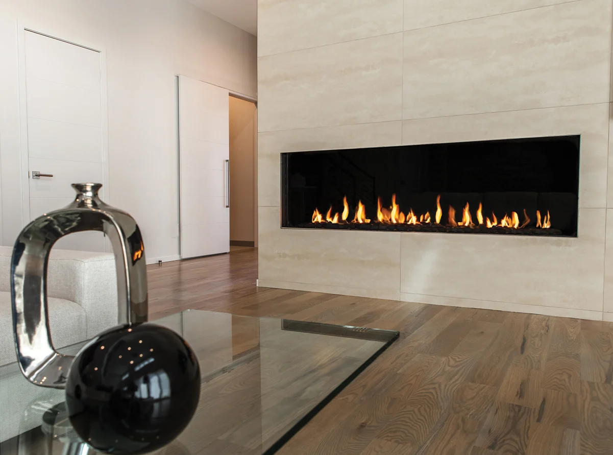 Modern gas Flare Front Facing 100" fireplace with 24" high glass, set into a large tiled wall in a minimalist living room. FLARE-FF-100H